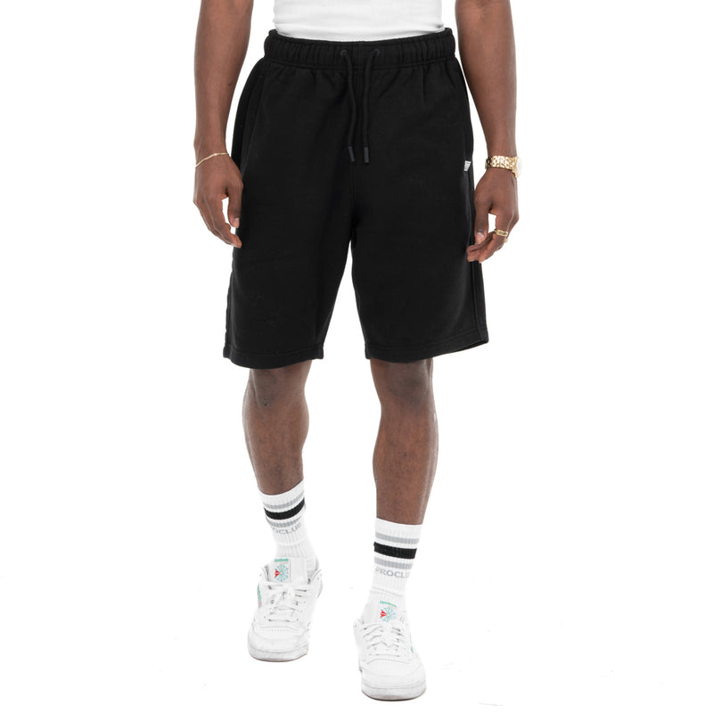Load image into Gallery viewer, Person wearing black sweat shorts with a black drawstring and two front pockets that sit at the knee on a white background
