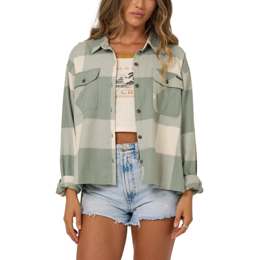 Woman wearing a plaid shirt over a graphic t-shirt with denim shorts on a plain background