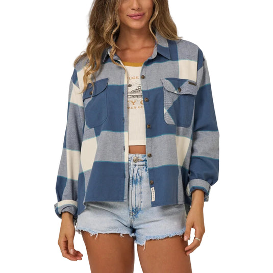 Woman wearing a blue and white plaid shirt over a graphic tee with denim shorts on a plain background