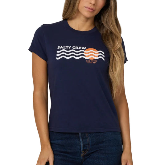 A woman modeling a navy blue short-sleeve t-shirt with a 'Salty Crew' graphic on the chest, paired with dark blue jeans, against a solid light gray background.