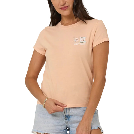 Woman wearing a peach t-shirt with a logo and denim shorts on a beige background