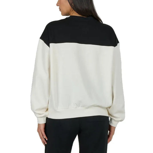 A woman viewed from the back wearing a color-block sweatshirt with a black yoke and an off-white body, paired with black pants, against a plain white background.