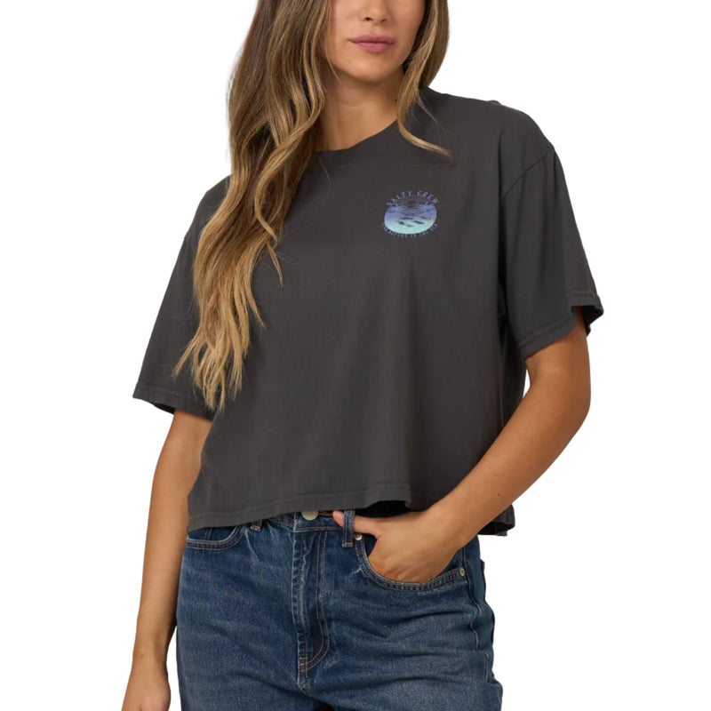 Load image into Gallery viewer, A woman modeling a dark charcoal gray cropped t-shirt with a small blue and white graphic on the left chest, paired with blue jeans, against a solid light gray background.
