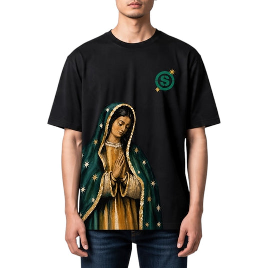 A man wearing a black t-shirt with a graphic print of Our Lady of Guadalupe and a green circular logo on the left chest, set against a plain white background.