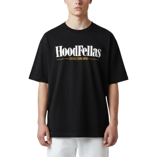 A model wearing a black oversized t-shirt with a white 'HoodFellas' graphic and gold text on the chest, paired with white pants, against a plain white background.