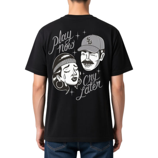 A man wearing a black short-sleeve t-shirt, viewed from the back. The shirt features a large white graphic print of a man laughing and a woman crying, with the text 'Play now cry later' and small star accents.