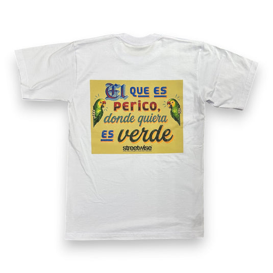 A white short-sleeve t-shirt with a yellow rectangular graphic on the chest featuring Spanish text and two green parrots, photographed against a plain white background.