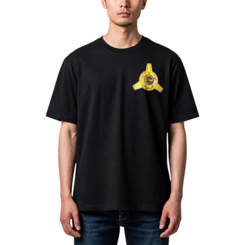Load image into Gallery viewer, A man wearing a black short-sleeve crewneck t-shirt with a yellow circular emblem printed on the left chest, paired with blue jeans, against a plain white background.
