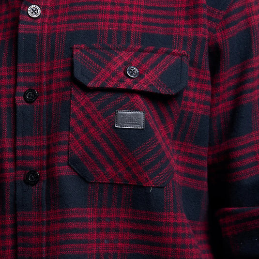 Close-up of a red and navy plaid flannel shirt with a chest pocket and a small leather brand patch reading 'SULLEN'.