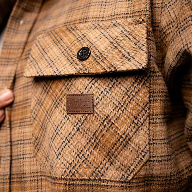 Load image into Gallery viewer, Close-up of a brown and tan plaid flannel shirt jacket pocket with a brown leather brand patch reading 'Sullen' and a black button.
