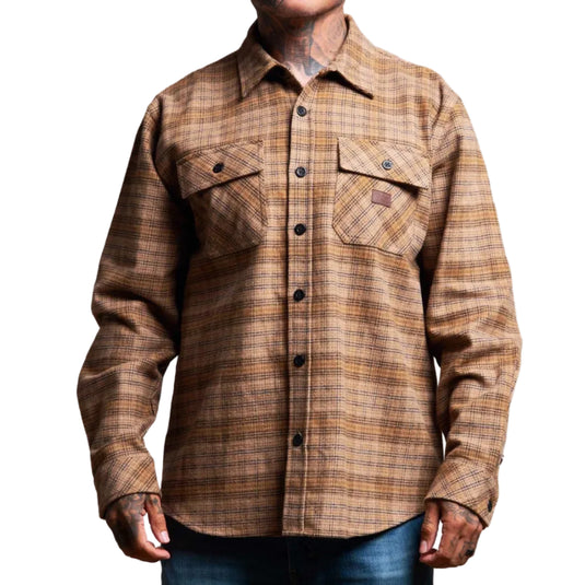 A man wearing a brown and tan plaid long-sleeve button-up shirt with two chest pockets, paired with blue jeans, shown from the neck down against a white background.