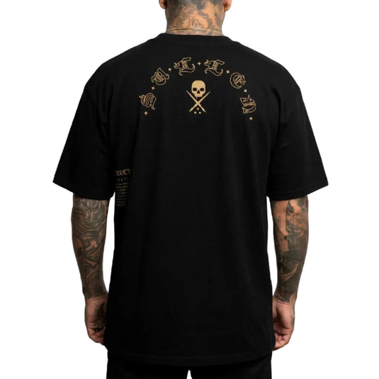 A man wearing a black t-shirt, viewed from the back. The shirt features a gold graphic print on the upper back with a skull and crossed bones in the center, flanked by gothic lettering, and additional small gold text on the lower left.