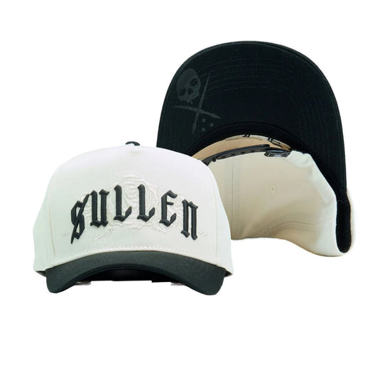 A white and black baseball cap with 'SULLEN' embroidered in black Gothic lettering on the front, shown alongside a black cap viewed from the back featuring a skull and crossbones graphic.