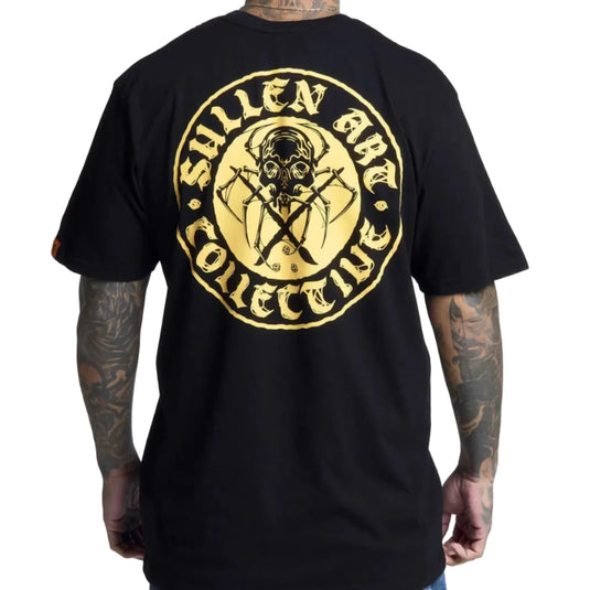 A man wearing a black t-shirt, viewed from the back. The shirt features a large circular graphic print in gold and yellow, depicting a skull with crossed tools and the text 'Sullen Art Collective'.