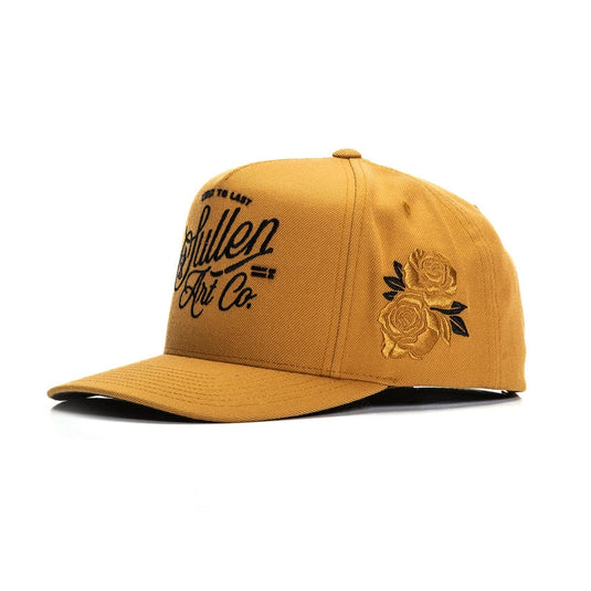 Camel colored cap with black embroidered design on the front panel and a camel embroidered rose patch on the left side of the hat on a white background