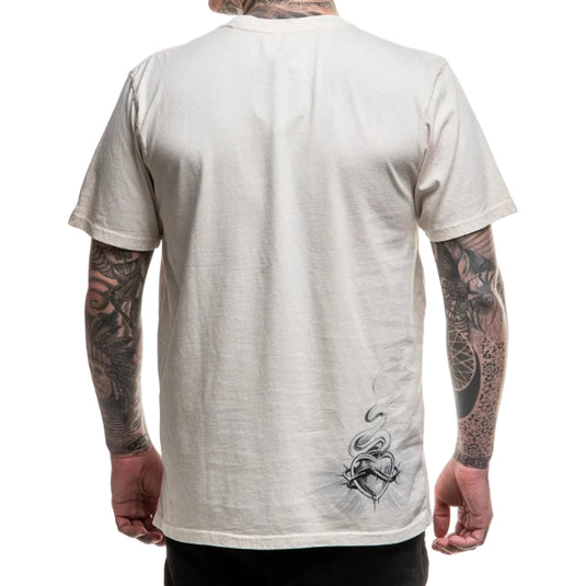 Person wearing a beige t-shirt with a design on the back, showing tattoos on arms.